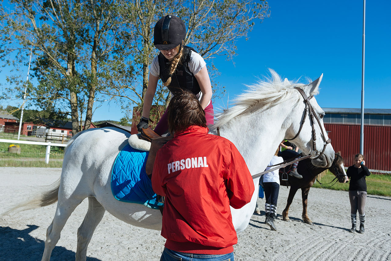 Personal hjälper elev att hoppa upp på ponny.